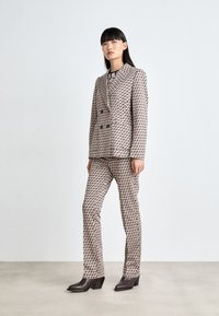 Doppelte Knopfleiste Blazer und eng anliegende Hose in einem geometrischen Muster in Rosa- und Brauntönen, kombiniert mit braunen, geschnürten Stiefeletten mit Absatz.