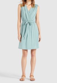 Robe portefeuille en tissu bleu clair, sans manches avec un décolleté en V, taille cintrée et ceinture à nouer. Se termine au-dessus du genou avec une texture douce.