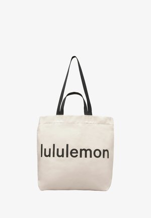 Borsa tote in tela color beige chiaro con logo "lululemon" nero e in grassetto. Caratterizzata da due manici neri e una superficie semplice, senza trama.