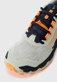 Scarpa atletica leggera con una tomaia grigia testurizzata, lacci blu navy e accenti arancioni. Presenta una suola in gomma resistente con modelli di trazione.