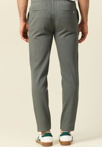 Grijze, taps toelopende broek met een gestructureerde afwerking, elastische tailleband, twee achterzakken, en gecombineerd met witte sneakers met groene accenten.