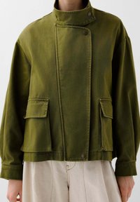 Olivengrün Baumwolljacke mit hohem Kragen, Druckknopfverschluss und zwei Vorderaschen; lockere Passform und strukturierten Stoff.