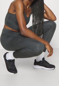 Scarpe da ginnastica nere con dettagli in mesh e texturizzati, abbinate a leggings grigi scuri e a una maglietta attillata, che mettono in risalto un design snello.