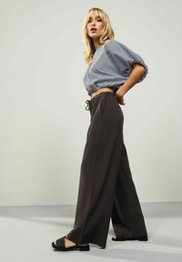 Sorte vide bukser med snoreliv, parret med en grå og hvid stribet cropped bluse. Modellen bærer sorte slidesandaler.