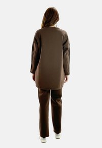 Brauner Oversize-Pullover und passende Hose, beide aus weichem Stoff. Das Outfit zeichnet sich durch eine lockere Passform aus und wird mit weißen Sneakers ergänzt.