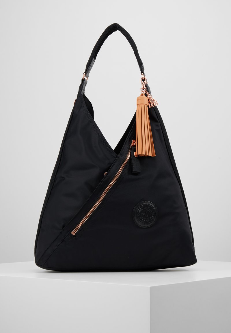 Black nylon handbag with an asymmetrical design, rose gold zipper, and a tan tassel attached to the side. Features a round logo patch.