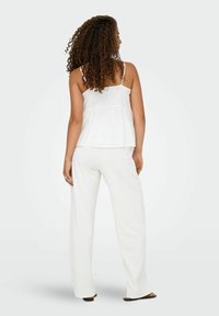 Witte mouwloze peplumtop gecombineerd met losse, wijde witte broeken. De outfit heeft een vloeiende textuur en verstelbare bandjes op de top.