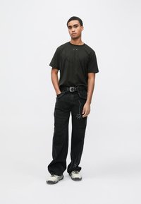 Camiseta negra con diseño sutil, combinada con jeans negros que presentan tachuelas decorativas y un cinturón. Usada con zapatillas gruesas.