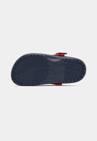 Red sandal with a navy rubber sole, featuring a textured bottom and wide strap with an adjustable buckle for secure fit.