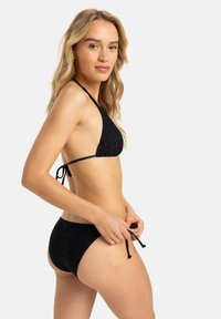 Completo bikini nero con un top triangolare testurizzato e allacciature, abbinato a slip a vita bassa. Il materiale è liscio e presenta un delicato motivo a griglia.