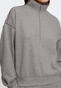 Felpa con zip grigia realizzata in materiale morbido. Presenta un colletto alto, una vestibilità ampia e polsini a coste con dettagli delle cuciture sottili.