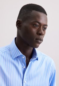 Camicia button-up azzurro chiaro con righe verticali bianche, dotata di colletto aperto e polsini con un bottone, realizzata in tessuto liscio.