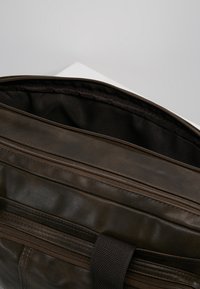 Braune Lederhandtasche mit einem Reißverschluss, die ein dunkelbraunes Innenfutter zeigt. Sie hat eine strukturierte Oberfläche und horizontale Reißverschlussfächer.