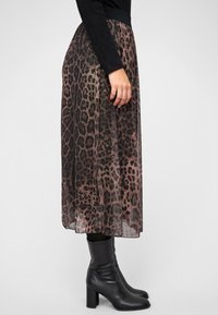 Leopardprint midi-jurk van doorschijnende stof met een zwarte tailleband, gecombineerd met zwart-kniehoge laarzen met een chunky hak.