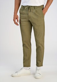 Olijfgroene chinos met een trekkoord in de taille, voorzien van twee zijzakken, een gladde textuur en een tapse pasvorm, gecombineerd met witte sneakers.