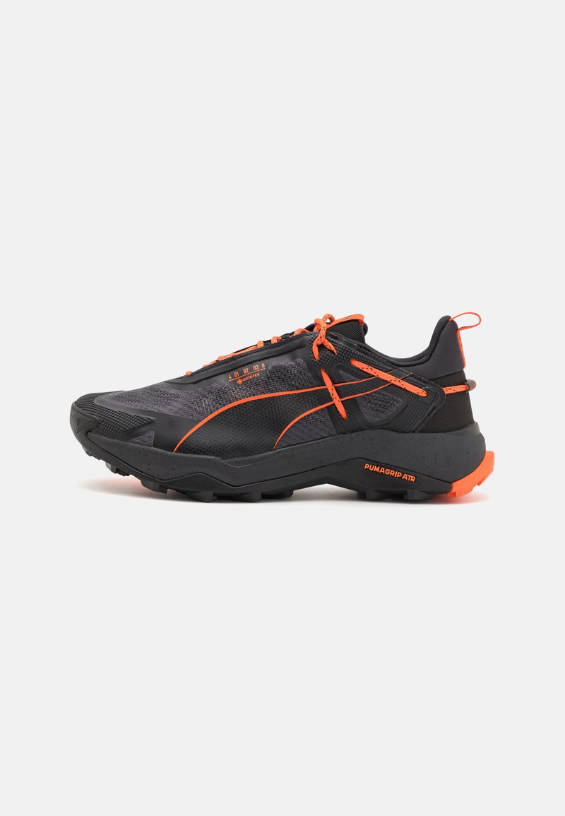 Baskets de sport noires et grises avec un dessus en mesh texturé, des accents orange et une semelle robuste marquée "PUMAGRIP ATR" pour une adhérence améliorée.