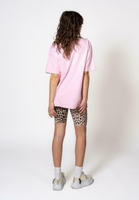 Pink oversized t-shirt paired with leopard print bike shorts. Model wears white sneakers and visible ankle socks. Smooth cotton texture.
