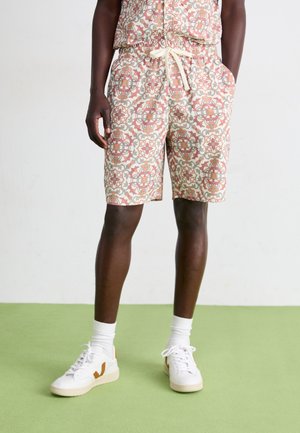 Shorts made of lightweight fabric feature a colorful geometric pattern in shades of peach, cream, and teal with an elastic waistband and drawstring.