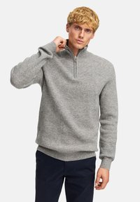 Pullover grigio a coste con colletto zip e maniche lunghe, caratterizzato da un tessuto testurizzato e un orlo dritto. Indossato sopra pantaloni scuri.