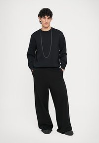 Μαύρο φούτερ με μακριά μανίκια, φορεμένο με φαρδιά μαύρα παντελόνια και μαύρα επίπεδα παπούτσια. Διαθέτει ασημένιο κολιέ αλυσίδας. Απλή, άνετη εφαρμογή.