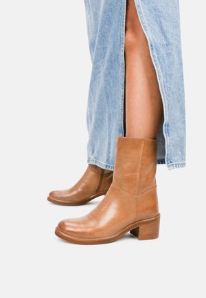 Brown leather ankle boots with a square toe, chunky heel, and smooth texture, paired with a light blue denim skirt featuring side slits.