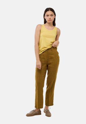 Un débardeur jaune sans manches associé à un pantalon en lin marron taille haute, fuselé. Des chaussures beiges à lacets, au design simple et à la texture lisse.