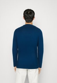 Maglione lavorato a maglia di color blu scuro, con scollatura rotonda, maniche lunghe e polsini a costine. Texture liscia con una silhouette aderente in vita.