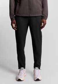 Zwarte broek van lichtgewicht materiaal, met een rechte snit en zijrits onderaan, gecombineerd met lichtgekleurde sneakers.