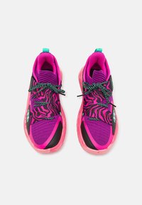 Lyserøde træningssko med en struktureret lilla overdel, sorte detaljer og grønne højdepunkter. Skoene har markante sorte og lyserøde bølkemønstre.