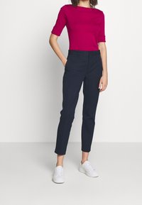 Ihanteellinen magentavärinen yläpaita lyhyillä hihoilla, yhdistettynä tummansinisiin kapeisiin housuihin ja valkoisiin lenkkareihin. Sujuva kangas, minimalistinen muotoilu.