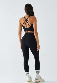 Czarny sportowy biustonosz z krzyżującymi się ramiączkami oraz dopasowane legginsy z wysokim stanem. Noszone z białymi i beżowymi sneakersami oraz paskowanymi skarpetkami.
