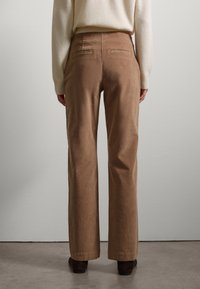 Brown corduroy wide-leg trousers with a smooth texture, featuring two back pockets and a subtle sheen, paired with a light sweater.
