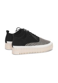 Zapatillas de deporte con diseño en blanco y negro, con una parte superior texturizada, cierre de cordones y una distintiva suela gruesa blanca. Presenta detalles acanalados en la suela.