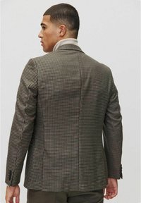 Marynarka w wzór houndstooth w ciemnym brązie i beżu. Dopasowany krój, jeden rozcięcie z tyłu i mankiety zapinane na guziki. Teksturowany materiał o sztywnej formie.