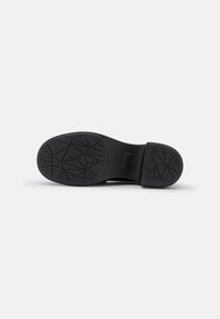 Semelle de chaussure noire présentant un motif de traction texturé avec des formes géométriques et une zone de talon lisse. Fabriquée en matériau caoutchouteux durable.