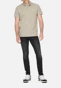 Polo-Shirt in hellbeige mit kontrastierendem Kragen und Besatz, kombiniert mit schwarzen Slim-Fit-Jeans und schwarz-weißen Sneakers.