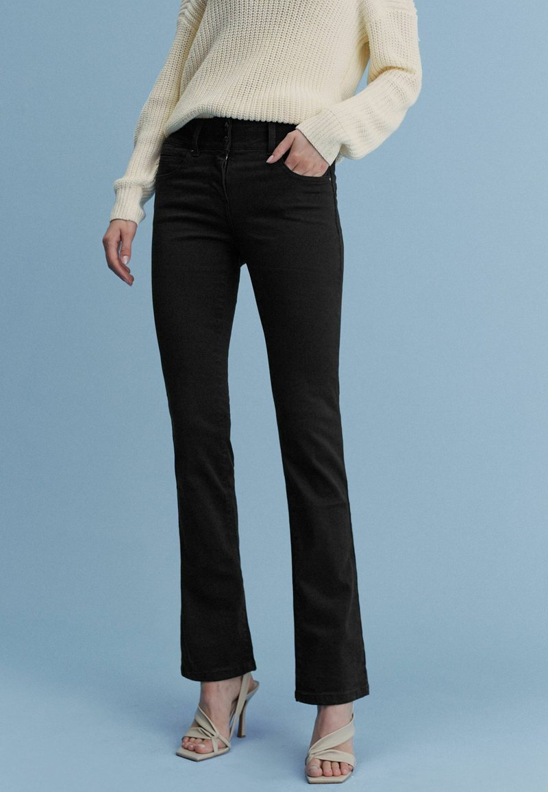 Zwarte flare jeans van denim met een gladde textuur, voorzien van voorzakken en een hoge taille, gecombineerd met een crèmekleurige gebreide trui.