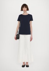 Haut bleu marine à manches courtes associé à un pantalon blanc large, des chaussures plates noires et un petit sac en bandoulière noir. Design simple et décontracté.