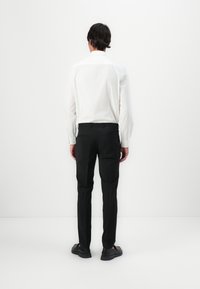 Camisa blanca de manga larga con yugo trasero, combinada con pantalones negros a medida y zapatos negros. Diseño limpio, tejido suave y forma ajustada.