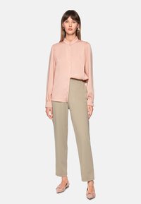 Blush pink long-sleeve blouse with buttoned collar, cream-colored trousers, and light pink flats. Smooth fabric and relaxed fit.