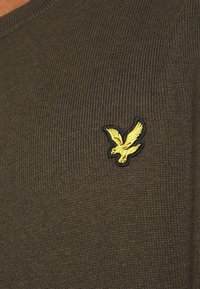 Maglione marrone lavorato a maglia con un logo ricamato di un'aquila gialla e nera sull'area sinistra del petto. Collo rotondo con texture a coste.