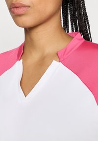 Baltas marškinėliai su rožinėmis raglan rankovėmis, su V formos iškirpte. Medžiaga atrodo lygi ir lengva, tinkama aktyviam dėvėjimui.