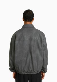 Szara kurtka z sztucznej skóry o luźnym kroju, z kołnierzykiem koszulowym i elastycznym pasem. Charakteryzuje się gładką fakturą i minimalnymi detalami szwalniczymi.