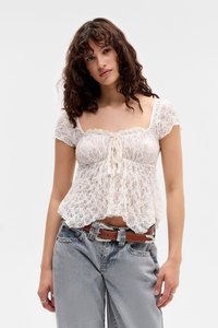 Blusa bianca in pizzo con scollatura quadrata, maniche corte a volant e nodo frontale. Abbinata a jeans azzurri a vita alta e una cintura marrone.