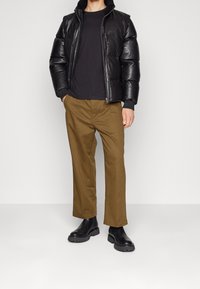 Svart puffjacka med dragkedja och texturerad yta, kombinerad med olivgröna byxor och svarta ankelstövlar med tjocka sulor.