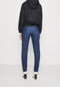 Chaqueta negra ligera con capucha y cintura elástica, combinada con vaqueros skinny de mezclilla azules y botas de tobillo blancas con tacón bloque.