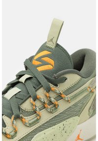 Baskets vertes et beiges avec des accents orange, lacets détaillés, logo brodé sur la languette et semelle intermédiaire mouchetée en gros plan.