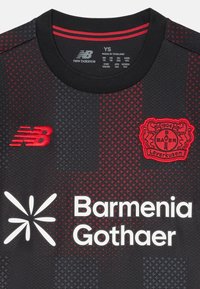 Camisola preta com detalhes em vermelho, apresentando um decote redondo, padrão texturizado, logotipo da New Balance, emblema do Bayer Leverkusen e texto de patrocinador.