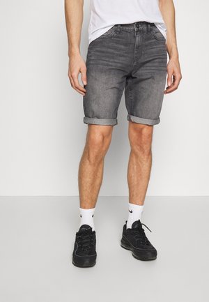 Pantalones cortos de mezclilla gris con dobladillos enrollados, que cuentan con cinco bolsillos y cremallera. Llevados con zapatillas negras y calcetines blancos.
