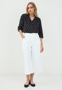 Blusa nera a pois con scollatura a V e maniche a tre quarti, abbinata a pantaloni bianchi larghi e cropped e ballerine nere.